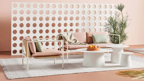 Blu Dot Dog Days Outdoor 2 Seat Sofa in Sunbrella Blush pink cushions with white powder-coated aluminum frame and all-weather rattan, styled with matching lounge chair and white side tables against a perforated breeze block wall