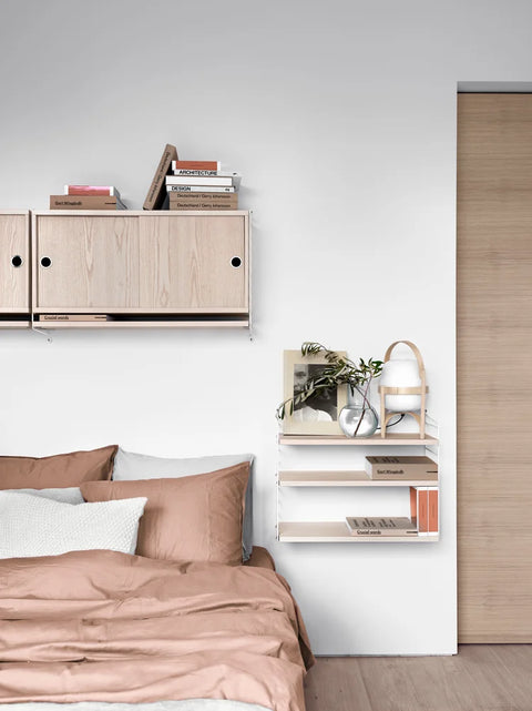 Ash String® Pocket shelf with white panels used as bedside storage next to a bed – modern Scandinavian modular shelving