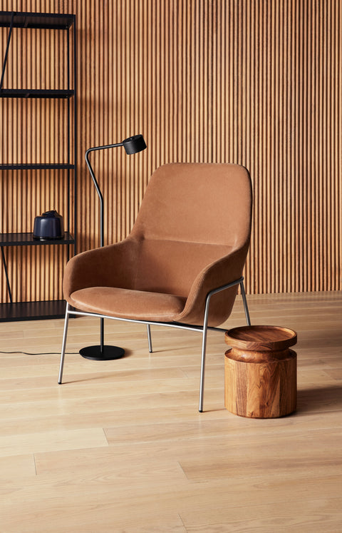 Blu Dot Acre Lounge Chair in camel velvet with brushed steel legs, styled in a warm wood-paneled reading nook with a black floor lamp and turned walnut side table