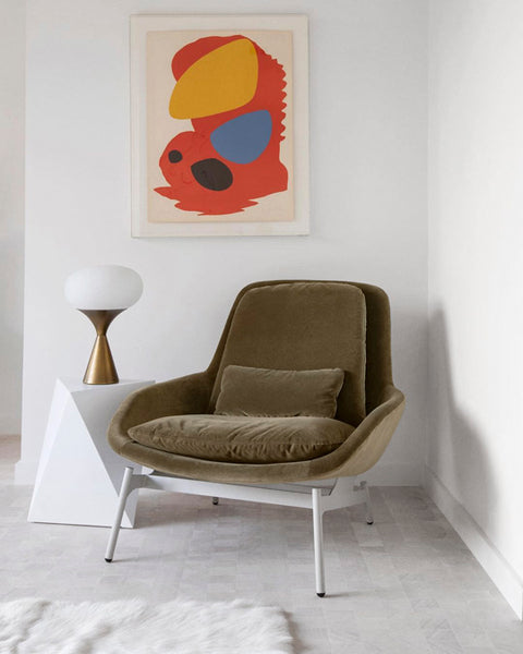 Blu Dot Field Lounge Chair in olive green velvet with white metal legs, styled in a bright white corner with a geometric side table, globe table lamp, and bold abstract wall art