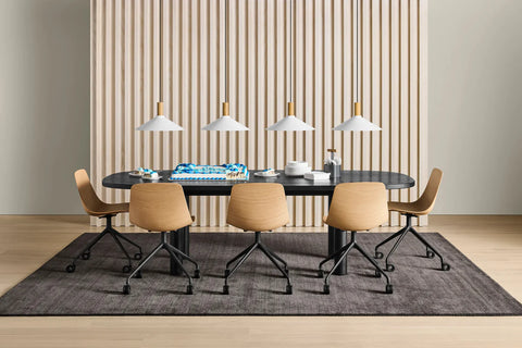 Blu Dot Clean Cut Task Chairs in white oak veneer with black powder-coated aluminum caster bases, styled around a black oval dining table with white pendant lights and fluted wood wall panel background