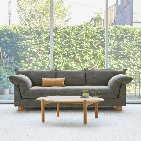 Gus* Modern Zoe Sofa, grey upholstered sofa with oak legs, Rosslyn Legacy beside a round wood coffee table by a large window