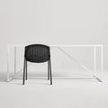 Black Hint Chair by Blu Dot with woven rattan seat and black steel frame, shown from behind at a white table