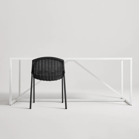 Black Hint Chair by Blu Dot with woven rattan seat and black steel frame, shown from behind at a white table