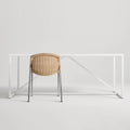 Natural rattan Hint Chair by Blu Dot with stainless steel legs, shown from behind at a white table