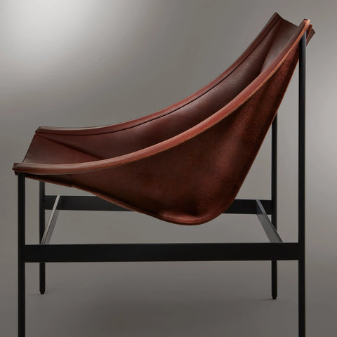 Side view of the Blu Dot Heyday Lounge Chair in chestnut leather highlighting the draped sling and black steel frame