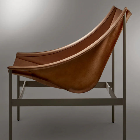 Side view of the Blu Dot Heyday Lounge Chair in sand leather with a light grey steel frame and sweeping sling silhouette