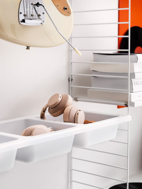 Close-up of String System white bowl shelf holding headphones, integrated with modular shelving in modern interior