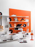 String System modular shelving in white with media shelf, styled with vinyl records, guitar, and retro electronics against orange backdrop