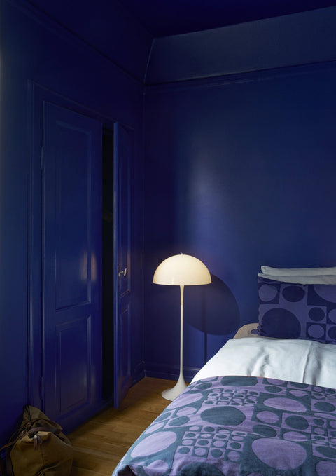 Louis Poulsen Panthella 400 Floor Lamp, white opal acrylic floor lamp, lit beside a bed in a deep blue bedroom