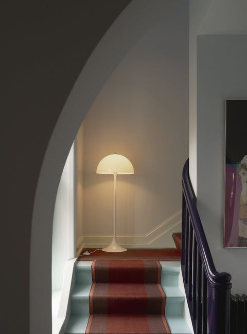 Louis Poulsen Panthella 400 Floor Lamp, white opal acrylic floor lamp, lit on a stair landing seen through an arched opening