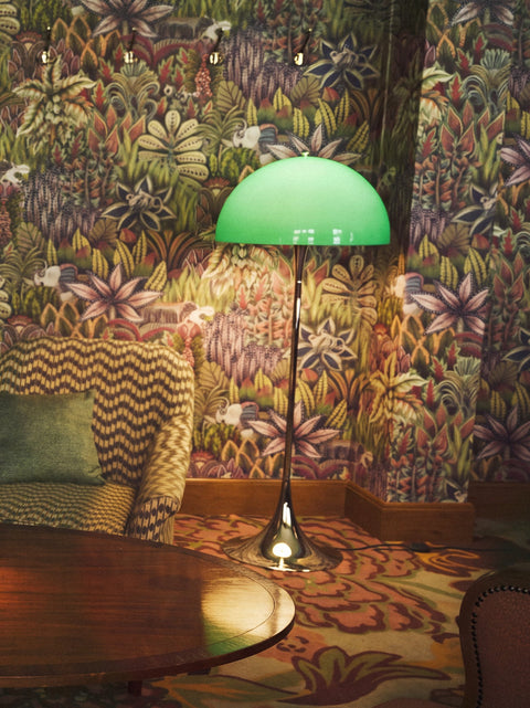 Louis Poulsen Panthella Floor Lamp, Original Opal Green floor lamp, lit against jungle wallpaper beside a round wooden table