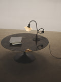 Louis Poulsen PH 1/1 Piano Table Lamp, Limited Edition, lit on a round dark stone coffee table beside a stack of books