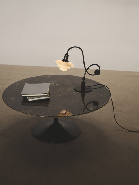 Louis Poulsen PH 1/1 Piano Table Lamp, Limited Edition, lit on a round dark stone coffee table beside a stack of books