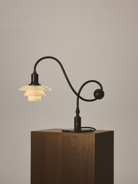 Louis Poulsen PH 1/1 Piano Table Lamp, Limited Edition, lit on a dark wood plinth, showing the curved stem and round counterweight