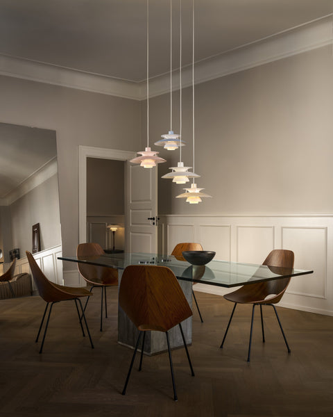 A cluster of Louis Poulsen PH 5 Opal pendant lights over a glass dining table with wooden shell chairs, in a grey room with panelled walls