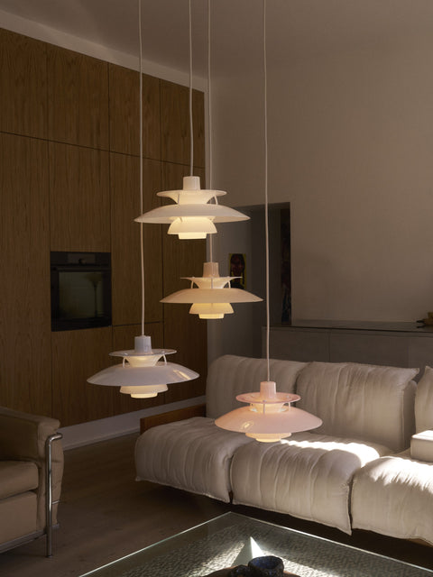 Four Louis Poulsen PH 5 Opal pendant lights lit at staggered heights above a cream sofa, beside a wood-panelled wall with a built-in oven