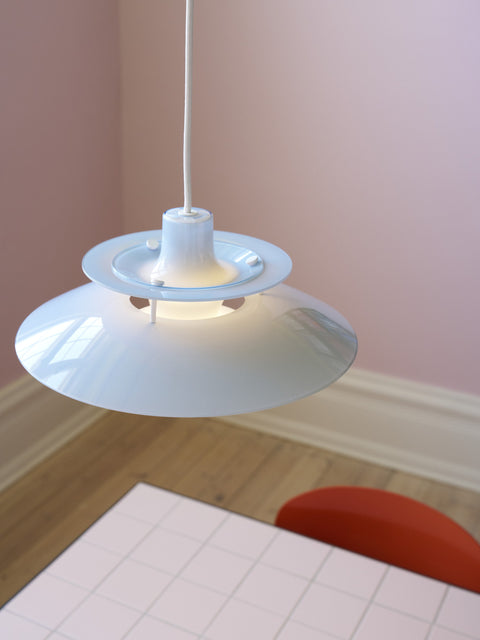 Louis Poulsen PH 5 Opal pendant light in Opal Pale Blue, lit and seen from above, hanging over a grid-tiled table in a pink room