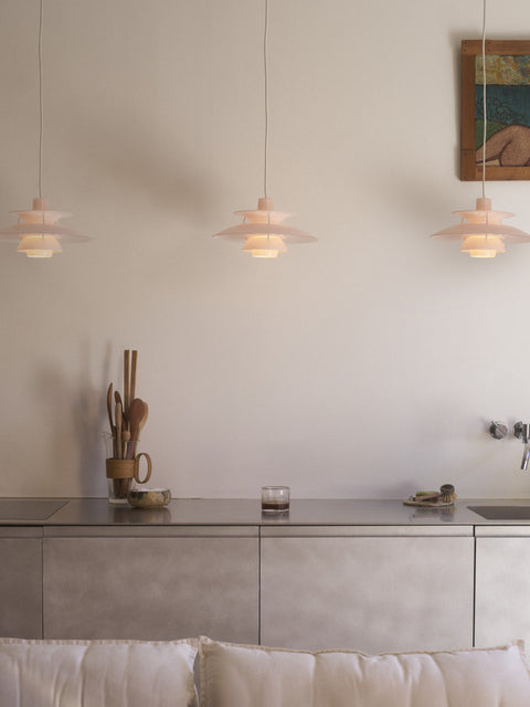 Three Louis Poulsen PH 5 Opal pendant lights in Opal Pale Rose, lit in a row above a steel kitchen counter against a pale wall