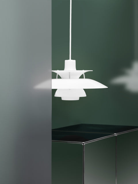 Louis Poulsen PH 5 Opal pendant light in Opal White against a dark green wall, beside a frosted glass panel and a green cabinet