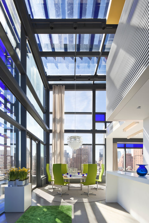 PH Artichoke chandelier in a sunlit modern dining area with floor to ceiling windows city skyline view and lime green chairs