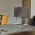 Pedestal Moon Tall TV Stand in Powder Blue, holding a flat screen in a concrete room with a wooden chair
