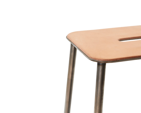Frama Adam Stool, close up of the rounded leather seat corner, its slot handle and the raw steel legs joining underneath