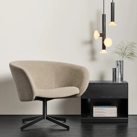Blu Dot Dally Nightstand in black, styled in a modern interior beside a beige bouclé swivel lounge chair with stacked Blu Dot design books on the lower shelf and a chrome vase on top, with black and glass pendant lights in the background
