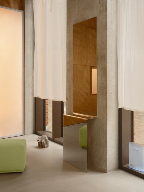 Pleat Mirror by Muuto in polished stainless steel styled in modern interior with concrete walls and Echo Pouf