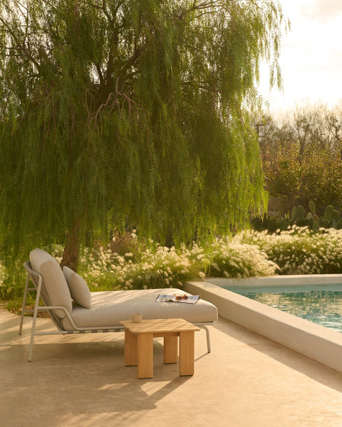 Side view of Muuto Settle Lounge Bed in laze grey with Assemble Coffee Table in teak, sunlit outdoor terrace