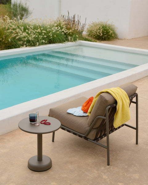 Muuto Settle lounge chair in taupe with matching linear steel side table by outdoor pool