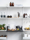 String System media shelf in anthracite, styled as a home bar with cocktail tools, glassware, ice block, lemon, and fresh ingredients