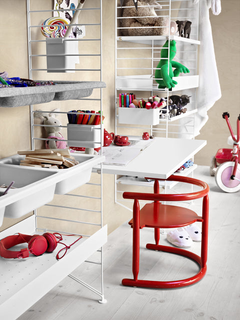 Children’s room with String System shelving in white featuring bowl shelves, storage, and a playful red chair