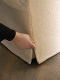 Audo Copenhagen Tearoom Chair, With Loose Cover, close-up of a hand pulling at the seam of the textured, light-colored loose cover on the base of the Tearoom Club Chair
