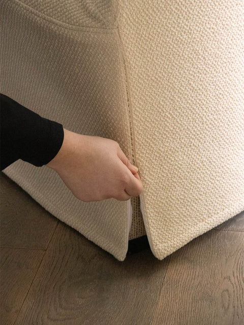 Audo Copenhagen Tearoom Chair, With Loose Cover, close-up of a hand pulling at the seam of the textured, light-colored loose cover on the base of the Tearoom Club Chair