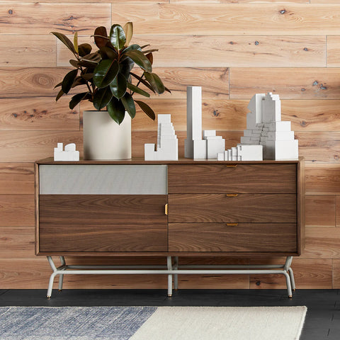 Blu Dot Dang 1 Door / 3 Drawer Console in walnut veneer with grey perforated steel door, styled in a modern room against a wood plank wall with a rubber plant and architectural white sculptures on top