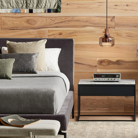 Blu Dot Construct Nightstand in Carrara marble top and black powder-coated steel frame, styled in a modern bedroom beside a grey upholstered bed with a vintage stereo receiver on top and amber glass pendant light above