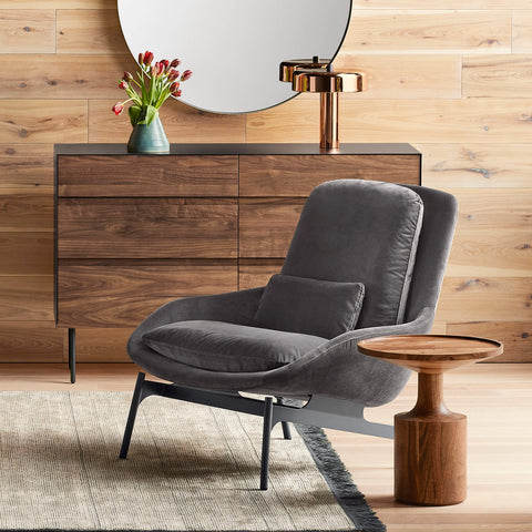 Blu Dot Field Lounge Chair in charcoal grey velvet with black legs, paired with a walnut side table, walnut dresser, and copper table lamp against a wood-paneled wall